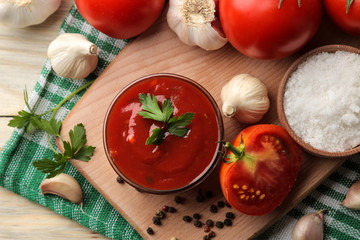 Red sauce or ketchup in a bowl and ingredients for cooking, tomatoes, garlic and spices on a natural wooden background. top view