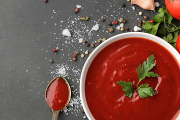 Red sauce or ketchup in a bowl and ingredients for cooking, spices, garlic, tomatoes and herbs on a black background. top view