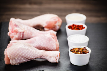 Raw chicken drumsticks on black stone on wooden background