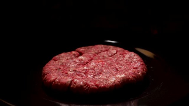 Close up of raw burger beef patty on black background, food and cooking concept. Stock footage. Fresh beef cutlet lying on a frying pan.