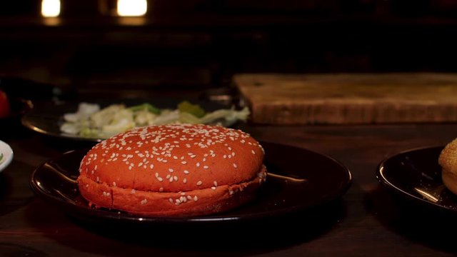 Burger buns on plates standing on wooden table in dark room before coooking process. Stock footage. Black and white burger buns with sesame seeds.
