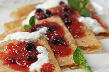 Macro shot of pancakes with berry jam and cream.  Pancakes are decorated with mint leaves.