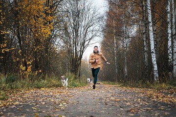 Fototapeta premium Cheerful guy running with dogs in nature