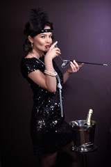 1920s retro style. Beautiful young woman in a dress and a fur cape posing in a chic interior looks...