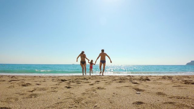 Happy family run on sand into the sea. Beach holiday. Slow motion.