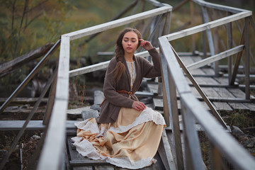 girl in vintage dress stands on a bridge