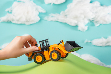 Kid's hand playing with a yellow toy truck driving in handmade world