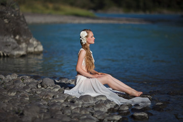  A girl in white clothes stands on a rocky shore near the river.