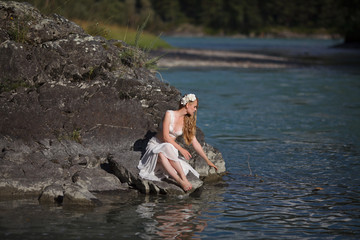  A girl in white clothes stands on a rocky shore near the river.