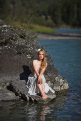  A girl in white clothes stands on a rocky shore near the river.