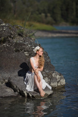  A girl in white clothes stands on a rocky shore near the river.