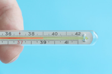 A medical/clinical mercury thermometer in person's hand showing the temperature of 39 °C. High temperature. Blue background. Theme of health care, medical treatment and disease prevention.