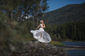  A girl in white clothes stands on a rocky shore near the river.