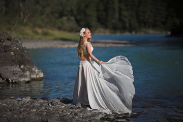  A girl in white clothes stands on a rocky shore near the river.