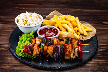 Grilled shashliks and French fries on black stone plate