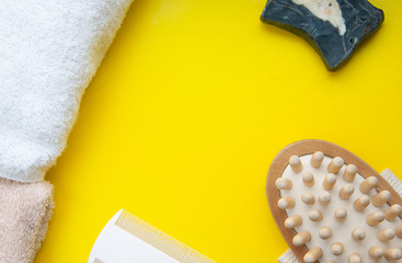 Anti-cellulite massage brush, scented soap, comb and towel on a yellow background. Bathroom accessoruies