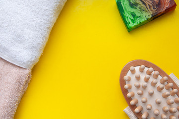 Anti-cellulite massage brush, fragrant soap and towel on a tellow background. Bathroom accessories
