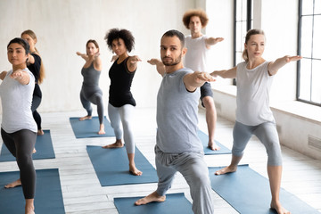 Fototapeta na wymiar Seven multiethnic people beginners practicing yoga performing Warrior II pose