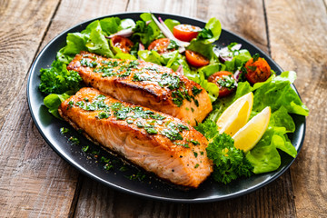 Fried salmon steaks with vegetables on wooden table