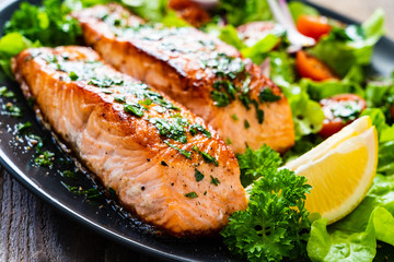 Fried salmon steaks with vegetables on wooden table