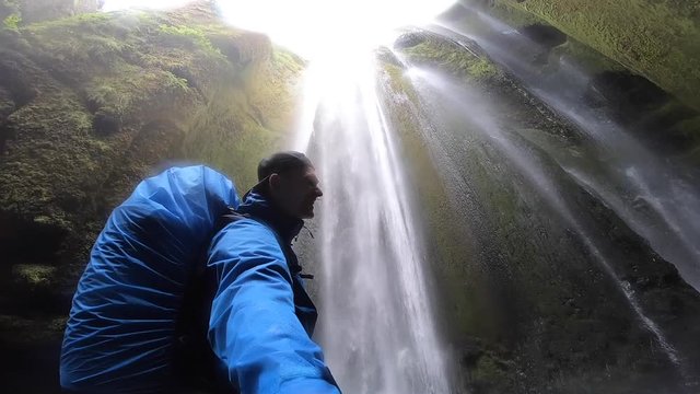 Backpacker exploring the famous touristic powerful waterfall Gljufrabui in the cave, slow motion, Iceland