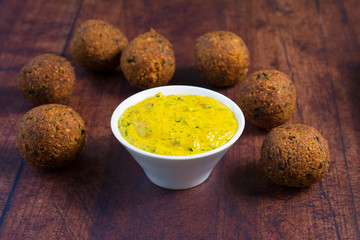 Tahini sauce made with turmeric powder, garlic and minced parsley leaves, in a white bowl. Vegan chickpea falafel placed around the bowl.