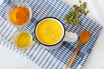 Healthy golden milk with turmeric and honey on white background and tissue. Diet, vegan and detox hot drink. Trendy drink. Copy space. Flat lay.