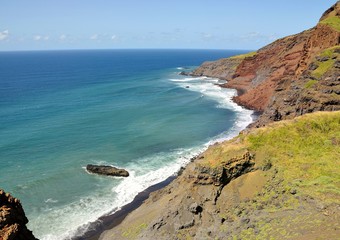 Waves crash on a black sand beach under rugged cliff