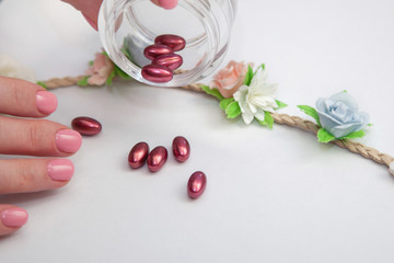 Obraz na płótnie Canvas care natural concept. the women hand with pink manicure hold glass jar with red pills on white background