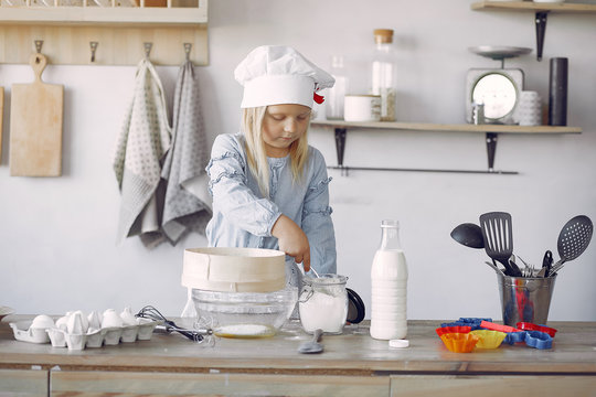 Child in a kitchen. Little girl with a dough. Kid in a blue shirt and white shef hat