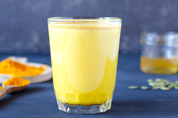 Healthy golden milk with turmeric and honey on a blue background and tiextile. Diet, vegan and detox hot drink. Trendy drink. Copy space. Flat lay.