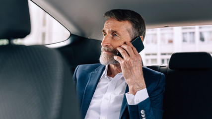 Serious businessman talking on cell phone sitting in taxi on backseat