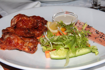 Sweet chicken wings with vegetables and rukala. Food on a white plate with milk sauce.