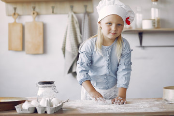 Child in a kitchen. Little girl with a dough. Kid in a blue shirt and white shef hat