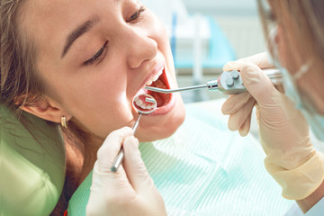 Girl sitting at dental chair with open mouth during oral check up while doctor. Visiting dentist...