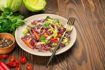 Bright salad of purple cabbage, white cabbage, bell pepper in a plate on a wooden table. Fresh vegetable salad. Food background. Vegetarian dish. View from above. Copy space.