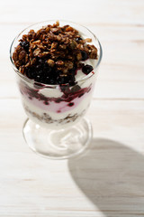 Yogurt parfait with cocoa granola and frozen blueberries. White wooden table, hard light, high resolution
