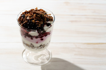 Yogurt parfait with cocoa granola and frozen blueberries. White wooden table, hard light, high resolution