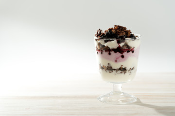 Yogurt parfait with cocoa granola and frozen blueberries. White wooden table, hard light, high resolution
