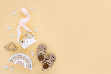 Wooden toys with rainbow, toy camera and cute baby slippers for kids on yellow background.  Set of gender neutral newborn accessories. Flat lay, top view