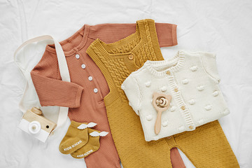 Set of  baby rompers and  knitted jumper on white bed. Gender neutral  baby clothes and accessories. Flat lay, top view