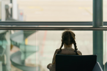 Child traveller in the airport. Trendy girl is ready to travel. Girl with two school braids sits in a chair in the departure lounge and wait for her flight. Flight delay concept. Touristic theme. © Yury and Tanya
