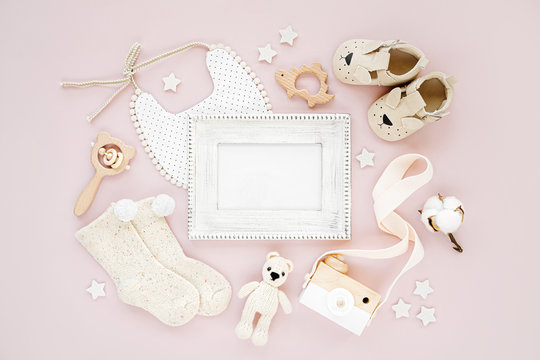 Photo frame with set of clothes and accessories fot newborn girl. Toys, socks and baby slippers with bib on pink background. Mock up tor text. Baby shower concept. Flat lay, top view