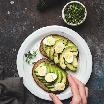 Hand picking avocado and quaill egg rye bread toast. Healthy food, clean eating concept