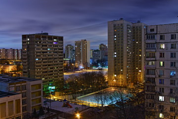 Beautiful multi-storey residential houses and yard stadium in the Moscow Konkovo area on winter night with amber glowing lighting and blue cloudy sky