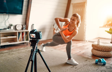 Athletic woman blogger in sportswear shoots video on camera as she does exercises at home in the...