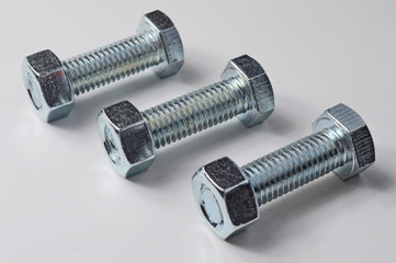 three bolts with nuts screwed on them. White background.
