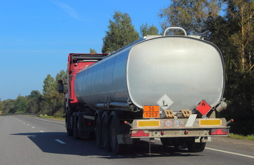Oil tank semi truck with grey barrel moving on suburban asphalt highway  road on a summer day blue sky and forest background, ADR dangerous cargo