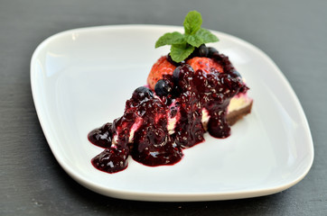 Delicious fruit strawberry and blueberry tart glazed by cherry sauce and fresh mint leaves on decorative white plate. Low depth of field.