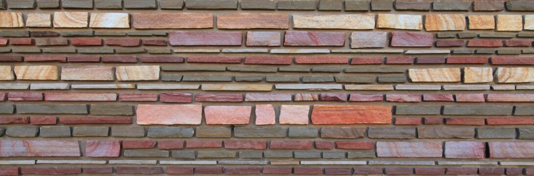 Surface and texture of multy-colored (colorful) decorative stone wall, background. Varicolored flat stones of regular shape in the wall construction. Modern fashionable design for the fences. Panorama